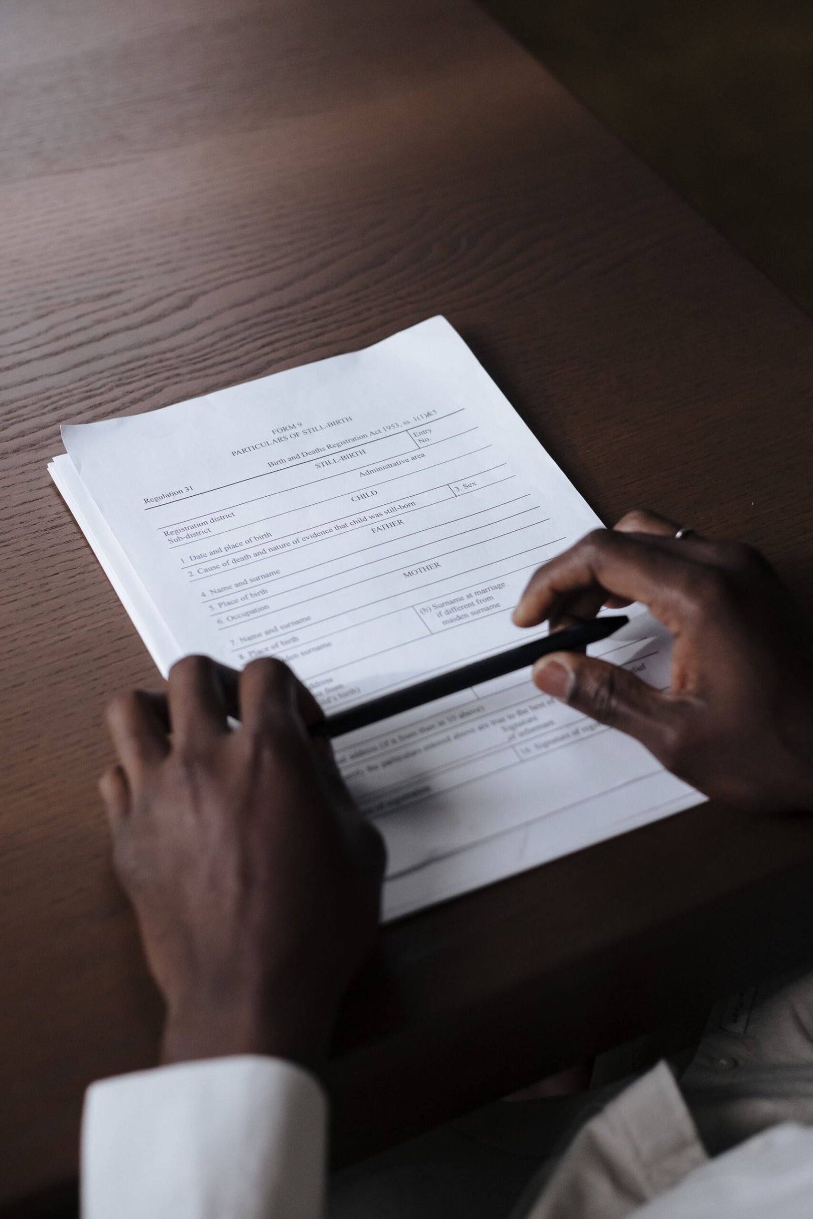 Hands holding a pen while reviewing documents on a wooden table